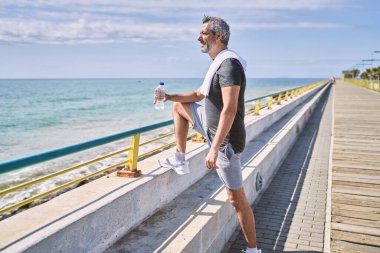 Orta yaşlı İspanyol bir adam, kendine güvenen, deniz kenarında spor giysileri giyen, gülümseyen.