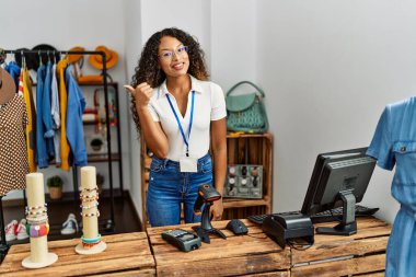 Güzel İspanyol kadın giyim mağazasında çalışıyor. Gülümsüyor, gülümsüyor. Başparmağıyla yana bakıyor ve işaret ediyor.. 