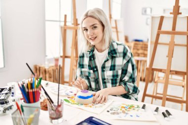 Sanat atölyesinde resim yaparken gülümseyen genç sanatçı kız..