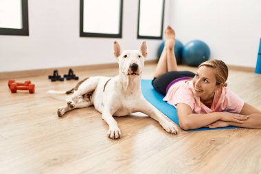 Beyazlı genç bir kadın spor merkezinde yoga minderine uzanmış kendinden emin bir şekilde gülümsüyor.
