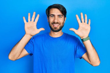 Gündelik kıyafetler giyen genç İspanyol adam on numarayı gösterip işaret ederken kendinden emin ve mutlu bir şekilde gülümsüyor.. 
