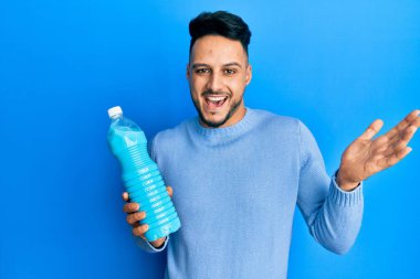 Genç Arap adam elinde deterjan şişesi tutarak başarıyı mutlu bir gülümsemeyle ve kazanan yüz ifadesiyle kutluyor. 