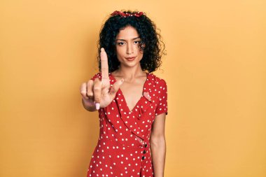 Yazlık elbise giyen genç Latin kız parmağını kaldırmış ve kızgın bir ifade takınıyor. 