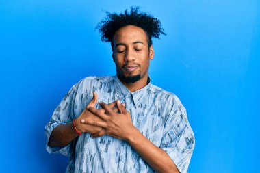 Sakallı, sıradan kıyafetler giyen, göğsünde elleri kapalı, yüzünde minnet ifadesi olan genç Afro-Amerikan bir adam. sağlık kavramı. 