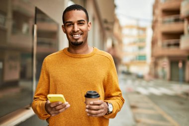 Genç Afrikalı Amerikalı adam akıllı telefon kullanıyor. Şehirde kahve içiyor..