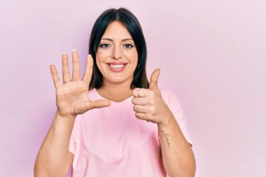 Gündelik pembe tişört giyen genç İspanyol kadın altı numarayı gösterip işaret ederken kendinden emin ve mutlu bir şekilde gülümsüyor.. 