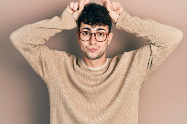 Gündelik kıyafetler giyen ve gözlük takan İspanyol genç adam boynuz gibi parmağıyla komik hareketler yapıyor. 
