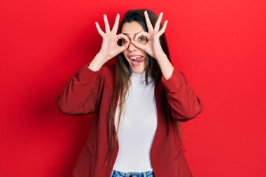 Genç esmer kız iş ceketi giyiyor dürbün gibi jest yapıyor, gözleri parmaklarından bakıyor. çılgın ifade. 