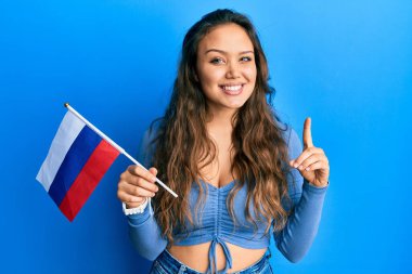 Rus bayrağını tutan genç İspanyol kız bir fikirle ya da soruyla gülümsüyor ve mutlu bir yüzle işaret ediyor. 