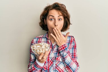 Genç esmer kadın elinde kabak çekirdekleri olan bir kâse tutuyordu. Ağzı elle kaplıydı. Şok olmuştu ve hata yapmaktan korkuyordu. şaşırmış ifade 