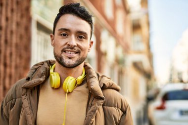 Şehirde kulaklık takarak mutlu gülümseyen genç İspanyol adam..