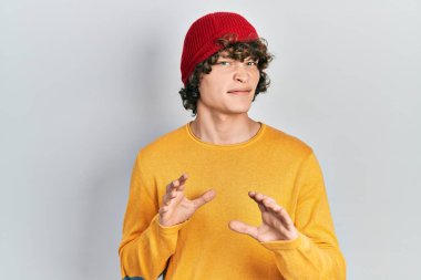 Tüylü şapka takan yakışıklı genç adam tiksindirici tepki verdiği için tiksinmiş ve ürkek bir ifade takınıyor. Eller havada. 