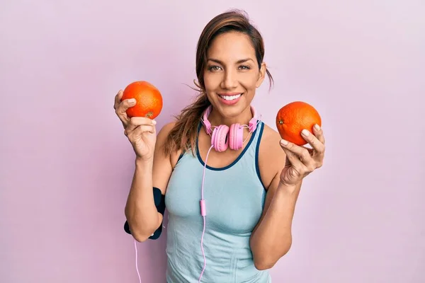 Mujer Latina Joven Usando Ropa Gimnasio Usando Auriculares Sosteniendo Naranjas —  Fotos de Stock