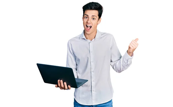 年轻的他的惊慌失措的生意人在工作时 用电脑笔记本电脑把大拇指指向旁边 笑着张开了嘴 — 图库照片
