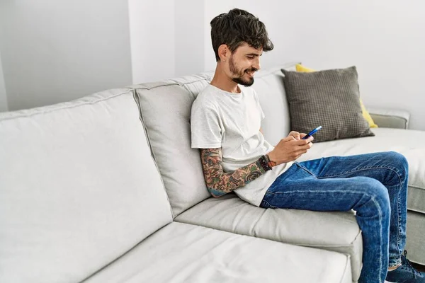 年轻的他的惊慌失措的男人坐在家里沙发上用智能手机 — 图库照片