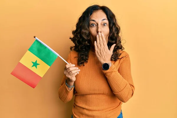 Латиноамериканка Средних Лет Держащая Сенегальский Флаг Прикрывающий Рот Рукой Шокирована — стоковое фото