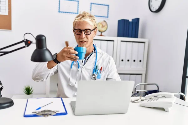 Młody Biały Mężczyzna Noszenie Lekarz Mundur Picie Kawy Klinice — Zdjęcie stockowe