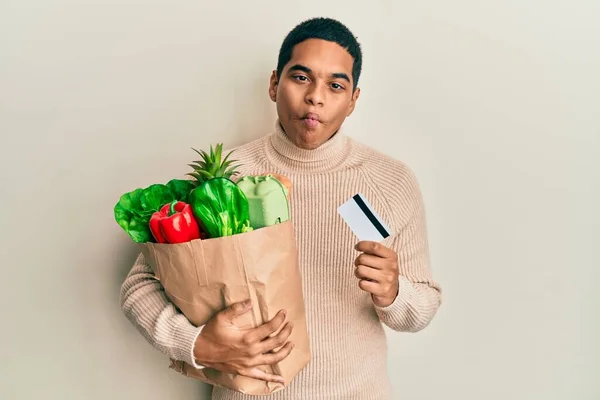 Joven Hombre Hispano Guapo Sosteniendo Comestibles Tarjeta Crédito Haciendo Cara —  Fotos de Stock