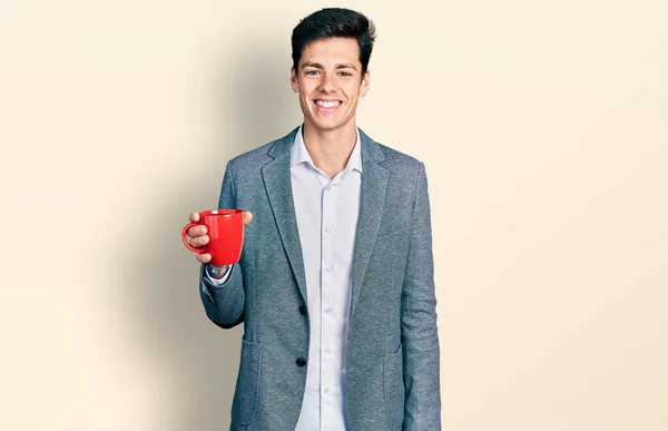 ビジネススタイルのコーヒーを飲むカップを身に着けている若いヒスパニックビジネスの男は肯定的で幸せな立っていると歯を示す自信を持って笑顔で笑顔 — ストック写真