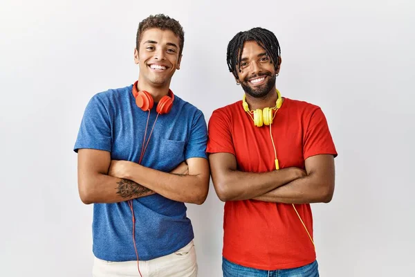 孤立した背景の上に立っている若いヒスパニック系の兄弟は カメラを見て交差腕で笑顔ヘッドフォン幸せな顔を着ています 正の人 — ストック写真