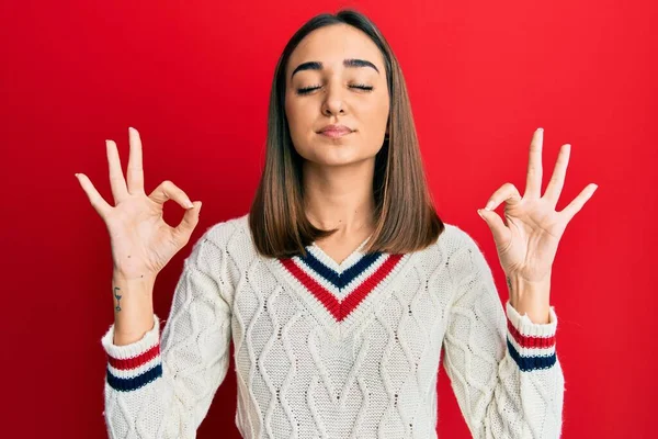 カジュアルな学生セーターを身に着けている若いブルネットの女の子はリラックスし 指で瞑想ジェスチャーを行う目で笑顔 ヨガのコンセプト — ストック写真