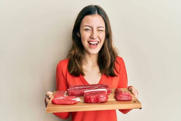 Joven Morena Sosteniendo Tablero Con Carne Cruda Guiñando Ojo Mirando —  Fotos de Stock
