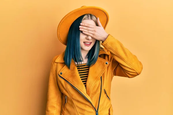黄色の帽子と革のジャケットを身に着けている若い現代の女の子は笑顔と驚きのために目をカバー顔に手で笑っています 視覚障害の概念 — ストック写真