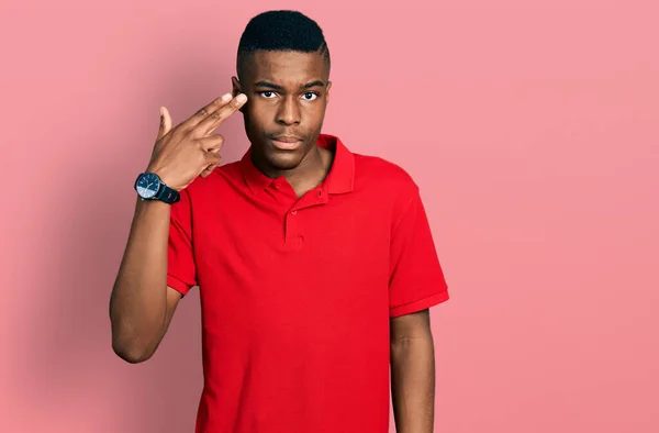 身穿休闲红T恤的年轻的非洲裔美国男人用枪指着自己的头和手指开枪自杀 — 图库照片