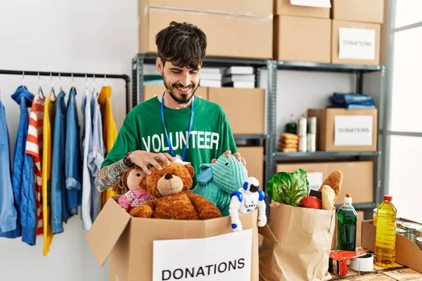 Jovem Hispânico Vestindo Uniforme Voluntário Segurando Caixa Doações Com Brinquedos — Fotografia de Stock