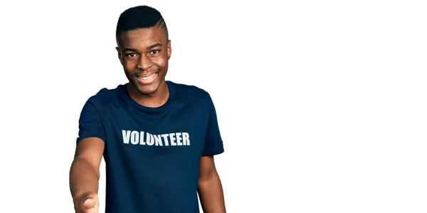 ボランティアTシャツを着た若いアフリカ系アメリカ人男性が笑顔でヤシの手を提供援助と受け入れ — ストック写真
