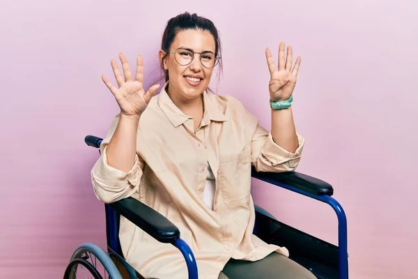 自信と幸せ笑顔ながら車椅子に座って指9番で指差す若いヒスパニック系の女性 — ストック写真