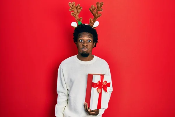 Young African American Man Wearing Deer Christmas Hat Holding Gift — Fotografia de Stock