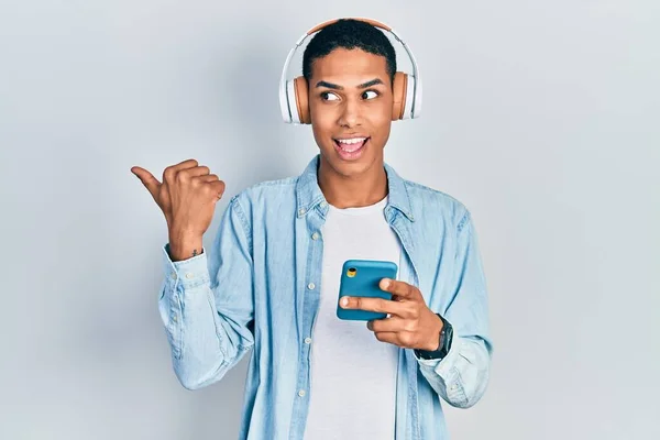 Молодий Афроамериканець Який Користується Смартфоном Навушниками Вказує Пальцем Бік Посміхаючись — стокове фото