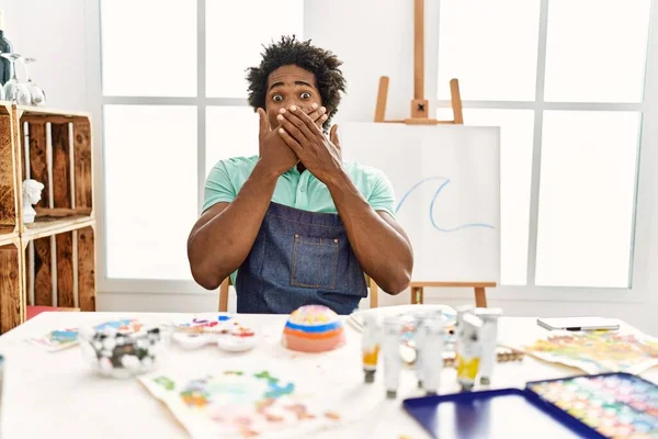 アートスタジオのテーブルに座っていた若いアフリカ系アメリカ人男性は 間違いのために手で口を覆いショックを受けました 秘密の概念 — ストック写真