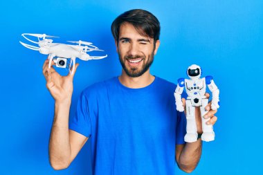 İHA ve robot oyuncak tutan genç İspanyol adam kameraya seksi bir ifadeyle bakıyor, neşeli ve mutlu bir yüzle.. 