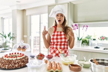 Güzel, genç, esmer pasta şefi kadın mutfakta hamur işleri pişirirken şaşkın şaşkın yukarı bakıyor, parmaklarıyla işaret ediyor ve kollarını kaldırıyordu.. 