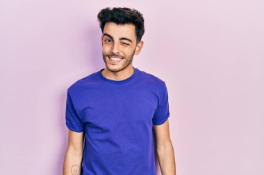 Gündelik tişört giyen genç İspanyol adam kameraya seksi bir ifadeyle bakıyor, neşeli ve mutlu bir yüzle.. 