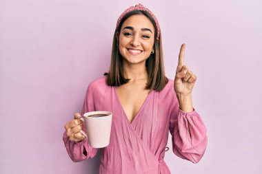 Genç esmer kız bir fincan kahve içiyor bir fikirle gülümsüyor ya da bir soru işareti yapıyor mutlu bir yüzle, bir numara 