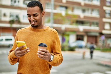 Genç Afrikalı Amerikalı adam akıllı telefon kullanıyor. Şehirde kahve içiyor..