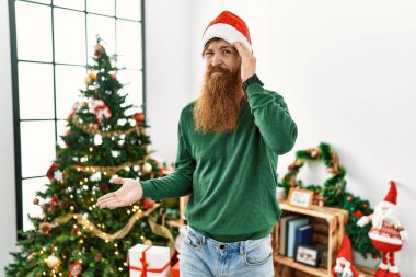 Uzun sakallı kızıl saçlı adam noel ağacı şapkası takıyor. Kafası karışmış ve avuç içi açık bir şekilde fotokopi alanını gösteriyor ve alnını işaret ediyor. Bunu bir düşün.. 