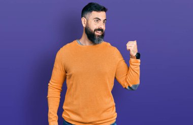 Sakallı, sıradan bir süveter giyen, mutlu yüzlü gülümseyen ve baş parmağıyla yüzünü gösteren İspanyol bir adam.. 