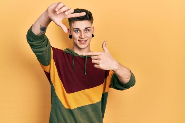 Kulakları genişlemiş, sıradan bir eşofman üstü giyen, elleri ve parmakları gülen yüzlü, çerçeveli beyaz bir çocuk. yaratıcılık ve fotoğrafçılık kavramı. 