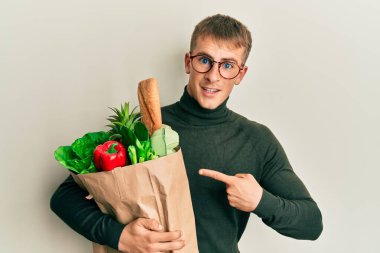 Elinde alışveriş poşeti olan genç beyaz bir adam mutlu bir şekilde elini ve parmağını gösterdi. 