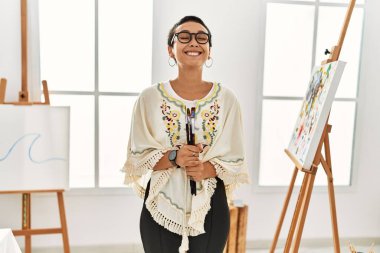 Resim stüdyosunda kendine güvenen genç İspanyol kadın fırça tutuyor.