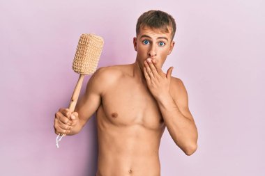 Genç, beyaz, üstsüz, duş süngeri tutan, ağzı elle kaplayan, şok olmuş ve hata yapmaktan korkan bir adam. şaşırmış ifade 