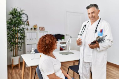 Doktor üniforması giyen orta yaşlı bir adam ve kadın klinikte tıbbi danışmanlık yapıyorlar.