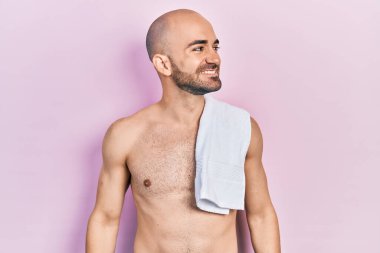 Tişörtsüz duran genç kel adam, yan bakmak, rahat profil pozu doğal yüz ve kendine güvenen bir gülümseme. 