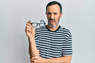 Orta yaşlı İspanyol bir adam günlük kıyafetler giyiyor ve elinde gözlük tutuyor. Bilgisi yok ve kafası karışık. şüphe kavramı. 