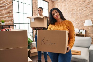 Karton kutularla dolu yeni bir eve taşınan genç çift yüzünde ciddi bir ifadeyle rahatlıyor. Basit ve doğal bir şekilde kameraya bakıyorsun.. 