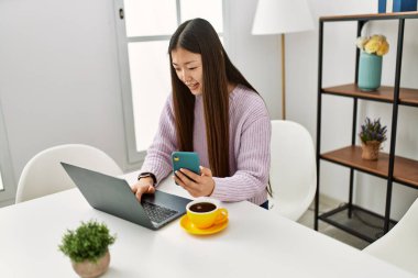 Laptop ve akıllı telefon kullanan Çinli genç bir kız evdeki masada oturuyor..